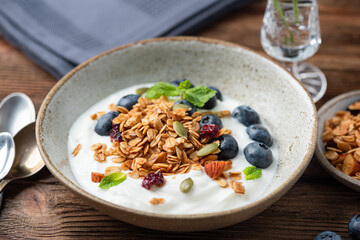 Bowl of yogurt with homemade granola and blueberries on a wooden table background, clean eating diet