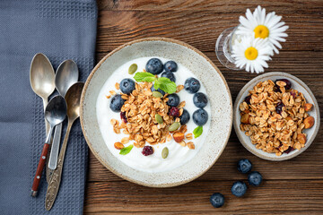 Bowl of yogurt with homemade granola and blueberries on a wooden table background, clean eating diet
