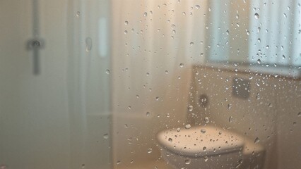 Rain on window glass with view of bathroom toilet in background