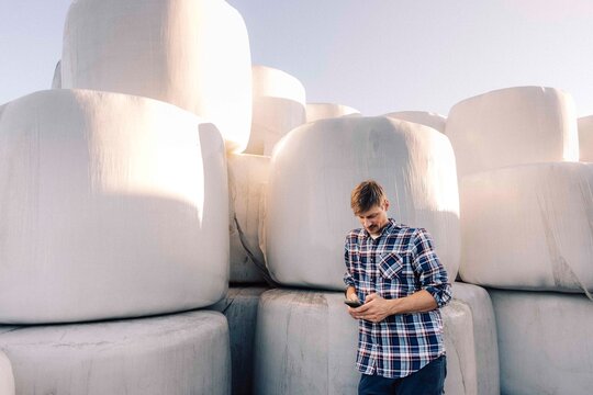 Male farmer using smart phone while leaning on hay stack in farm