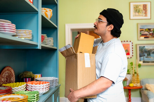 Salesperson holding cardboard box while looking at shelf stacked with crockery at home decor shop