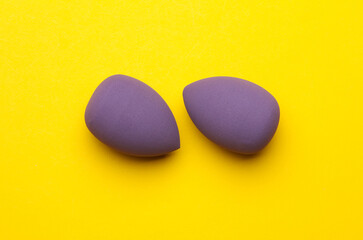 Makeup eggs shape blenders of purple color on yellow background. Beauty concept. Top view