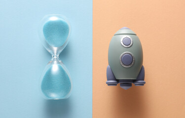 Toy space shuttle and hourglass on pink blue background. Startup, education, business concept