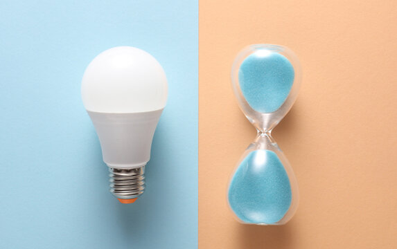 Hourglass with led light bulb on pink blue background. Creative idea. Top view