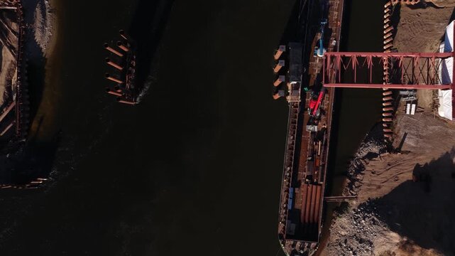 Vertical aerial image of a bridge foundation construction site on a riverbank, showing rebar, formwork, steel piles, and machinery within a sheet pile cofferdam.