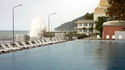 A rainy day at a seaside resort. A swimming pool with a few swimmers in the rain on the hotel grounds. A stormy sea.