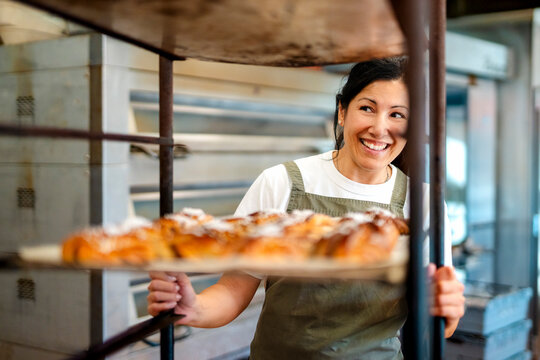 Happy female baker pushing trolley loaded with cinnamon buns