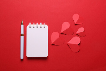 White notebook and paper hearts on red background. Love, romantic, Valentine's day concept