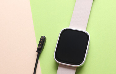 Smart watch with charging cable on color background