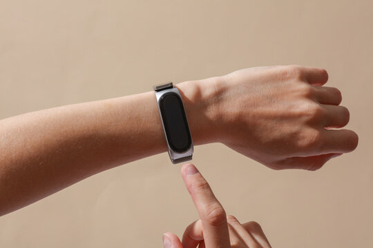 Female hand with modern smart bracelet on wrist, beige background