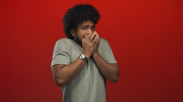 Man expressing fear against vivid red background showing apprehensive gestures with isolated setting.