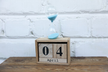 Wooden calendar cubes organizer with date april 4 and hourglass on wooden table