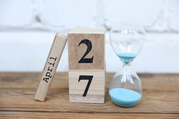 Wooden calendar cubes organizer with date april 27 and hourglass on wooden table