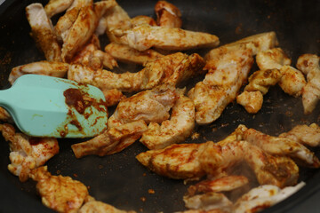 Pieces of chicken fillet meat are fried in a frying pan