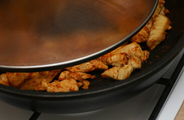 Pieces of chicken fillet meat are fried in a frying pan