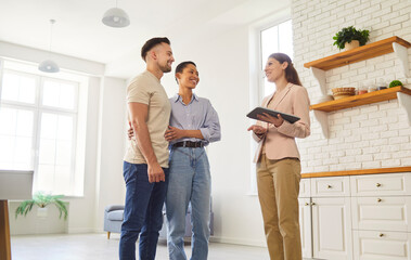 Realtor and young married couple standing inside spacious, modern kitchen, getting professional real estate services, discussing modern design trends with designer woman. Home buying, property tours