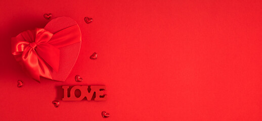 Valentine’s Day background with red heart-shaped gift box, satin ribbon bow, and word LOVE on...