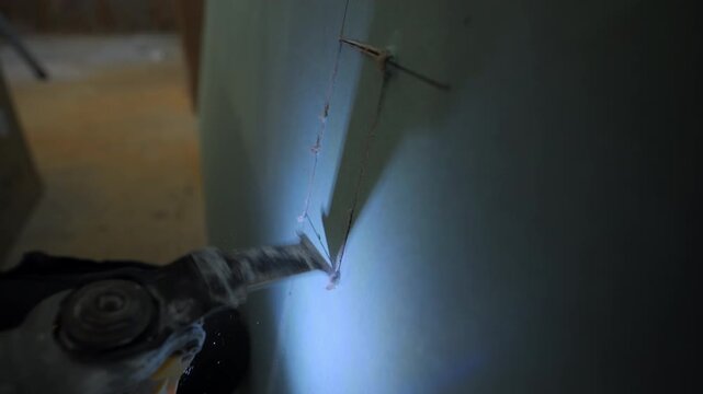 Close-up shot of the construction worker using an oscillating multi-tool to cut a rectangular opening in drywall. Dust particles are visible as the blade slices through.