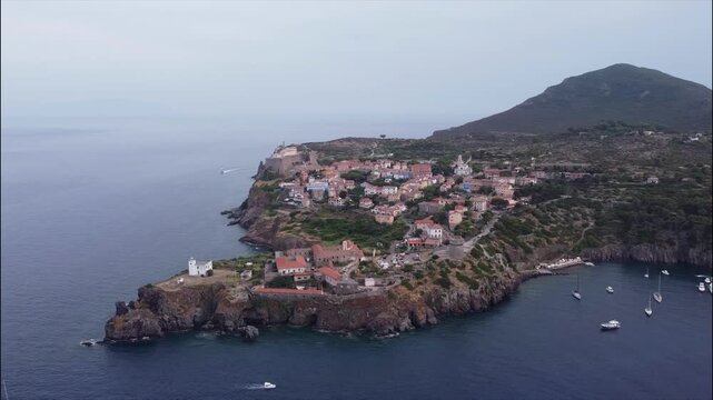 Aerial view of the historic town of Capraia Isola, Livorno, Tuscany, Italy. Colorful houses on a rocky cliff surrounded by the Mediterranean Sea.