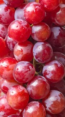 A close-up view of a cluster of shiny, plump, reddish-purple grapes, dripping moisture