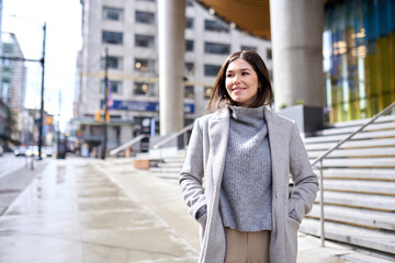 Young happy elegant brunette woman wearing coat standing on big city street. Smiling business lady...