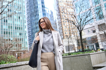 Smiling business lady walking outdoors looking away enjoying fall time in downtown. Young happy...