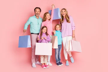 Fotobehang Sportwinkel Happy family shopping day with parents and children posing with colorful bags against a pink background  © deagreez