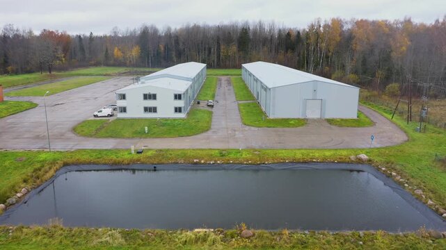Valka, Latvia - October 29, 2025: Aerial view of industrial buildings with surrounding greenery, camera pans to reveal expansive scene development