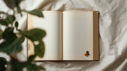 Open book with blank pages on a white sheet with plant in the foreground creating a sense of calm