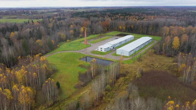 Valka, Latvia - October 29, 2025: Aerial view of industrial complex surrounded by autumn foliage, camera pans closer to reveal details of buildings