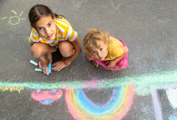A child draws a house and a rainbow on the asphalt with chalk. Selective focus.