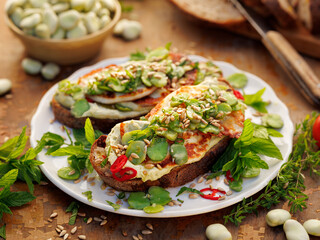 Sandwiches with broad bean spread and grilled goat cheese sprinkled with roasted sunflower seeds and fresh mint on a ceramic plate, close-up view