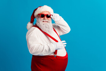 Santa in red suspenders with hat and beard poses playfully against a blue background for Christmas marketing and holiday fun