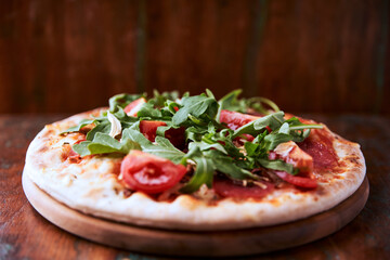 Pizza with salami, tomatoes and mozzarella cheese and arugula. Rustic wooden background. Soft focus. Copy space.	