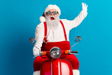 Santa on a bright red scooter waves hello in a festive Christmas scene against a blue background
