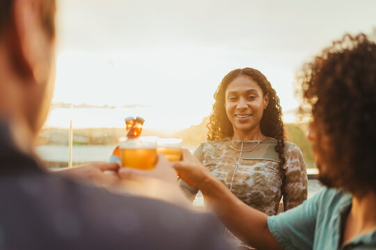 Young Latino and Hispanic adults toasting with beers on a terrace at sunset. They are enjoying a relaxing and joyful moment together. 