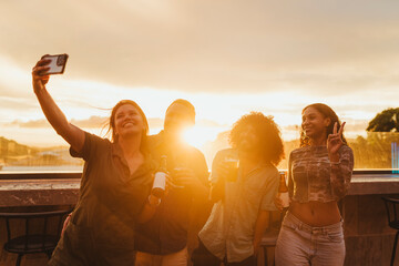 Young friends taking a selfie together at sunset with drinks in hand