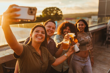 Friends taking a selfie while celebrating with drinks at sunset