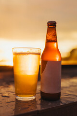 Chilled beer bottle and glass at golden hour with sunset reflections