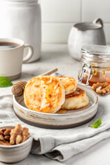 Cottage cheese pancakes or syrniki with walnuts and honey on ceramic plate on light gray kitchen table. Healthy sweet breakfast