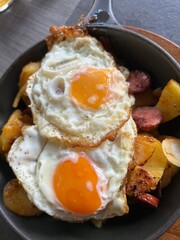 Two fried eggs with fried potatoes top view in cast iron pan