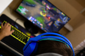 Dynamic low angle view of enthusiastic gamer in blue headphones communicating with teammates during intense online match. Warm home atmosphere with vibrant keyboard lighting
