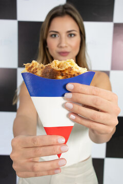 jovem mulher com um crepe na m&atilde;o em primeiro plano, comendo um crepe ou panqueca em fundo quadriculado preto e brando com roupa clara