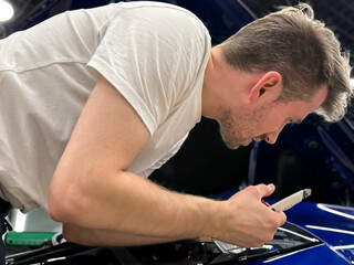 Car wrapping, detailing, tuning and styling. Detailer smoothes PPF. PPF protective film against chips and scratches. A car wrapping specialist applies a polyurethane film to the car. Selective focus.