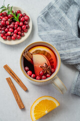 A hot cranberry Christmas drink in a mug on a light  background with cinnamon, berries and napkin.