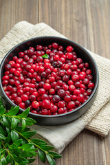 Fresh cranberries in a dark bowl on a wooden background with green branch and napkin.