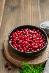 Fresh cranberries in a dark bowl on a wooden background with green branch and napkin.