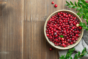 Fresh cranberries in a dark bowl on a wooden background with green branch and napkin.