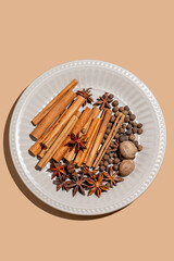 Various spices on a plate against a bright beige background with shadows.