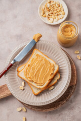 Peanut butter toast on a plate on a light background with scattered nuts, spread and knife.